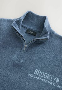 Pusiau užtrauktuko puloveris iš mėlyno meliro audinio, su nertiniu apykakle ir subtiliu užrašu "BROOKLYN" priekyje. Sidabrinis užtrauktukas.