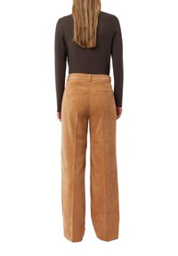 Brązowa bluzka z długim rękawem połączona z wysokim stanem, szerokimi spodniami z sztruksu w ciepłym, jasnobrązowym kolorze. Spodnie mają tylne kieszenie i teksturowane wykończenie.