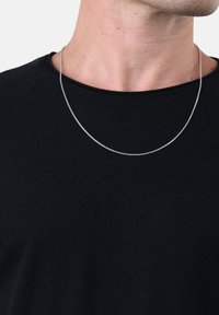 Collana in argento con un design delicato e sottile, appoggiata su una camicia di tessuto scuro, caratterizzata da una finitura liscia e lucida.