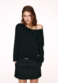 Pull noir à mailles larges avec un design épaules dénudées, manches larges et texture douce, associé à une jupe noire.