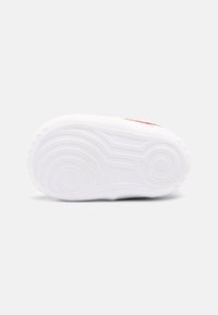 Sole obuvi z texturované bílé gumy, se soustřednými kruhovými vzory a drážkami pro trakci, s mírným růžovým akcentem poblíž paty.