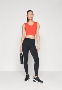 Rød ermeløs crop top med Nike-logo, kombinert med svarte høytaljede leggings. Svarte joggesko og en metallisk vannflaske.