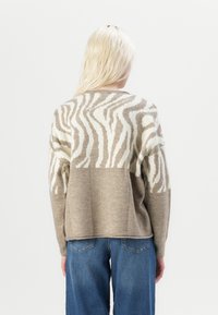 Zebra-patterned sweater in beige and cream, featuring a relaxed fit and long sleeves. Soft texture with contrast detailing on the sleeves.