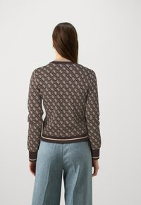Brown patterned sweater with cream motifs, ribbed hem and cuffs, fitted silhouette, paired with light blue wide-leg trousers.