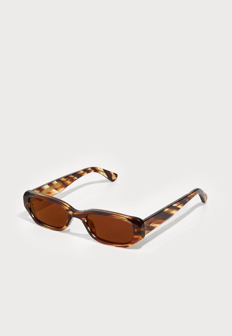 Lunettes de soleil en écaille de tortue avec des montures angulaires et des verres marron. Les branches présentent un motif rayé et ont une finition brillante.