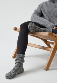Calcetines de punto grises y negros con un diseño holgado, tejido texturizado y un puño acanalado, usados con leggings negros en una silla de madera.