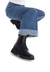 Stivali stringati in pelle nera con suola in gomma spessa. Jeans con orli arrotolati in denim azzurro. Focus sulle calzature e sulle gambe.
