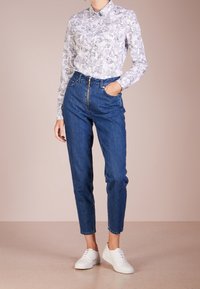 Weißes gemustertes Hemd mit Kragen, kombiniert mit hochtaillierten blauen Jeans und weißen Sneakers.