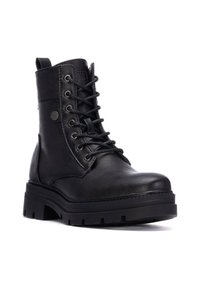 Botas de tobillo de cuero negro con seis ojales, suela robusta y tirador. Presentan una textura suave y un sutil detalle de logo en el lado.