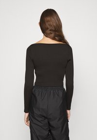 Maglietta nera a maniche lunghe con scollatura larga e arrotondata, design aderente e texture liscia, abbinata a pantaloni neri larghi.