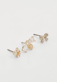 Trois paires de boucles d'oreilles : une avec de petites perles, un design en forme d'abeille orné de cristaux transparents, et une en forme de nœud décorée de strass. Accents en métal doré.