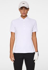 Witte poloshirt met een gestructureerd ontwerp, korte mouwen en een drieknopenlijst, gecombineerd met zwarte broek en een witte pet met een logo.