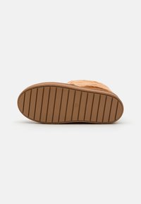 Botte en suède beige avec un dessus texturé, dotée d'une épaisse semelle en caoutchouc avec des rainures horizontales pour une meilleure traction. Forme globalement arrondie.