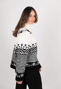 Knitted sweater in black and white featuring a high neck, geometric patterns, and textured detailing; loose fit with ribbed cuffs and hem.