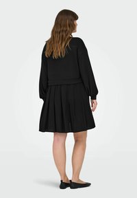 Top nero a maniche lunghe con gonna plissettata; tessuto morbido e strutturato; vestibilità rilassata con vita stretta; scarpe nere piatte alla caviglia.