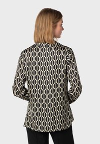 Blusa a maniche lunghe con un motivo circolare nero e beige, dal taglio dritto e realizzata in un tessuto morbido, con cuciture visibili e un dettaglio con spacco sul retro.