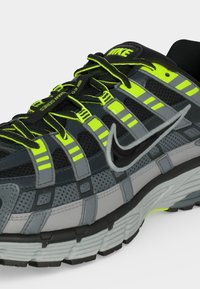 Μαύρο και γκρι παπούτσι τρεξίματος Nike με νέον κίτρινες πινελιές, ανακλαστικές ρίγες, παχύ πάτο και ορατό λογότυπο Nike στο πλάι.