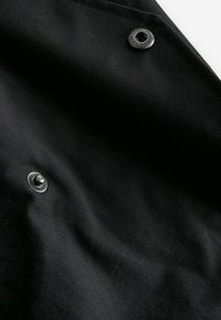 Tissu noir avec deux boutons-pression métalliques noirs, l'un partiellement ouvert, montrant des plis subtils et des détails de couture.