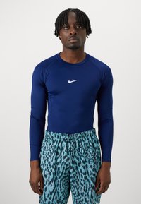 Marineblaues langärmliges Sportoberteil mit weißem Logo und türkisfarbenen Leopardenmuster-Shorts. Der Stoff wirkt glatt und dehnbar.