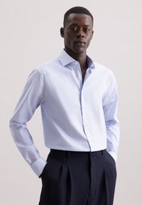 Camicia azzurro chiaro con sottili righe bianche, maniche lunghe e colletto alla francese, abbinata a pantaloni scuri su misura.