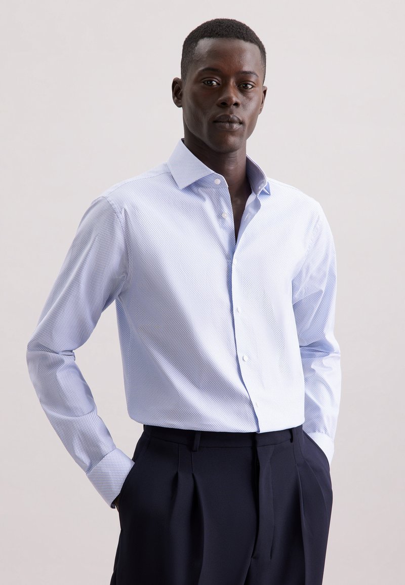 Camicia azzurro chiaro con sottili righe bianche, maniche lunghe e colletto alla francese, abbinata a pantaloni scuri su misura.