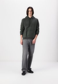Hanorac verde din fleece cu un buzunar frontal, asortat cu blugi gri cu croială largă și adidași negri. Design simplu, stil casual, textură moale.
