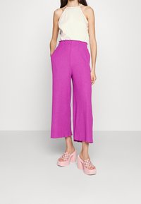 Vida byxor i stark rosa linne, med en samlad midja och en avslappnad passform. Sätts ihop med ljusrosa platåskor med rutmönster.