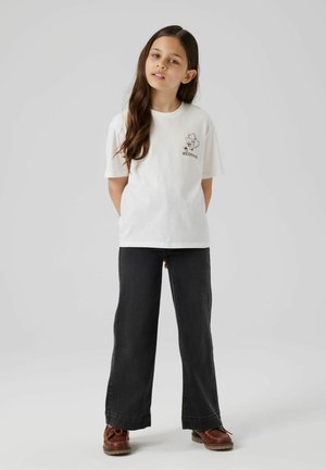 White cotton t-shirt with short sleeves, featuring a chest graphic. Paired with black wide-leg jeans and brown lace-up shoes.