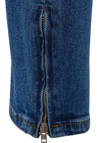 Jean en denim avec une fermeture éclair latérale ; tissu bleu, couture visible en orange et une finition texturée. La fermeture éclair court verticalement le long de la jambe.