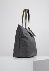 Czarna nylonowa torba na ramię o gładkiej fakturze, z dwoma ciemnymi skórzanymi uchwytami i skórzaną klapką, na białym postumencie.