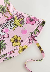 Bob rose avec imprimé tropical comprenant des palmiers, des fleurs d’hibiscus jaunes et roses, des étoiles de mer, des cerises et le mot « Cherry Coke ».