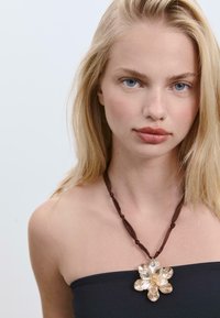 Collana con nastro marrone che presenta un grande pendente floreale realizzato con materiali traslucidi, con forme simili a petali e un centro texturizzato.