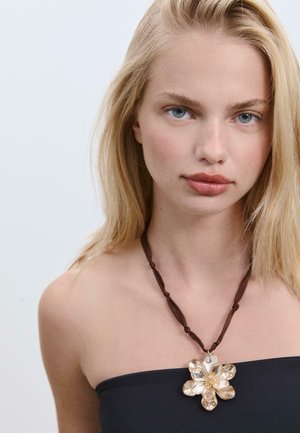 Collana con nastro marrone che presenta un grande pendente floreale realizzato con materiali traslucidi, con forme simili a petali e un centro texturizzato.