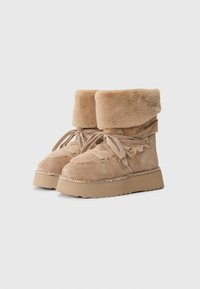Krásné béžové ankle boots z veluru s umělou kožešinou kolem kotníku, plochou gumovou podrážkou, dekorativními stříbrnými prvky a látkovými tkaničkami. Texturovaný povrch na svršku.