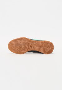 Zapatilla deportiva con parte superior negra y acentos turquesas, que cuenta con una suela de goma texturizada de color marrón y un agarre con patrón.