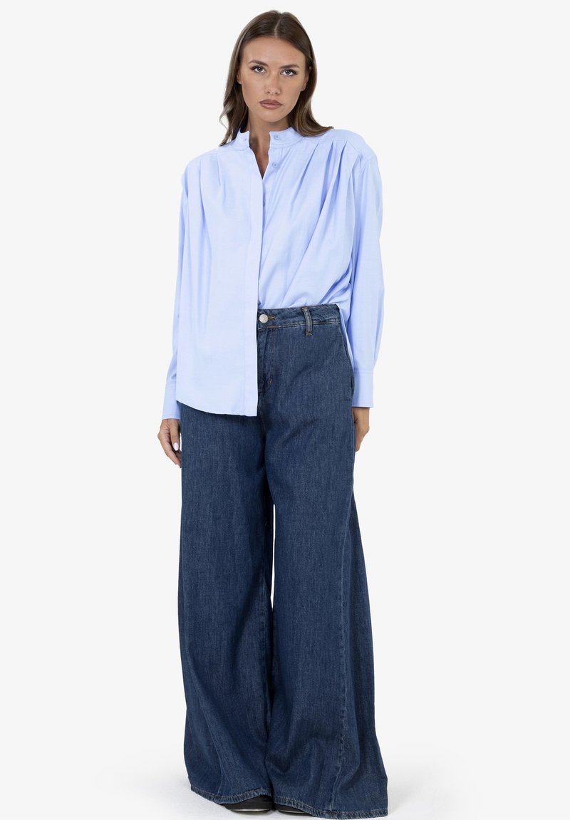 Lichtblauw shirt met lange mouwen en een mandarijnkraag, gecombineerd met losse, donker denim wijde pijpen jeans. Eenvoudig ontwerp, gladde textuur.