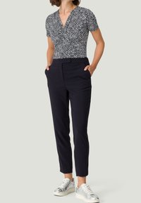 Haut à motifs noir et blanc à manches courtes, associé à un pantalon tailleur bleu marine et des baskets argentées, avec des poches latérales.