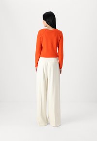 Orange sweater with long sleeves, round neck, and ribbed hem paired with white, wide-leg trousers featuring two back pockets.