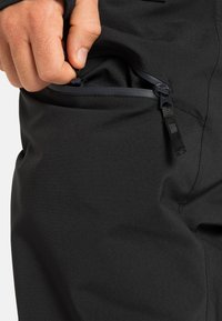 Met de hand de ritszak op zwart stoffen kleding open trekken, waardoor de gladde binnenvoering en de rits trekker zichtbaar worden.