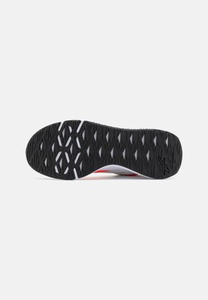 Podeszwa buta do biegania z czarnym bieżnikiem i geometrycznymi wycięciami odsłaniającymi białe warstwy pod spodem, pokazująca wzór przyczepności i logo marki.