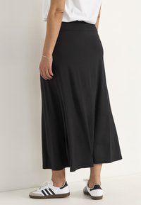 Zwarte enkel-lange rok van zachte stof, met een glad oppervlak en een elastische tailleband, gecombineerd met witte sport schoenen.