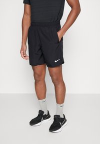 Mustad spordipüksid elastse vöökohaga, küljetaskud ja väike valge Nike logo. Kandmisel hallid sokid ja mustad spordijalatsid.