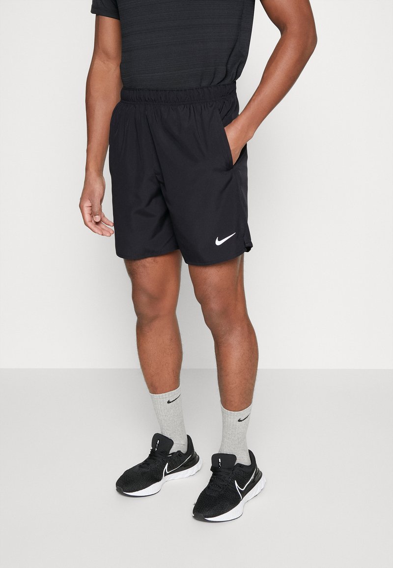 Mustad spordipüksid elastse vöökohaga, küljetaskud ja väike valge Nike logo. Kandmisel hallid sokid ja mustad spordijalatsid.