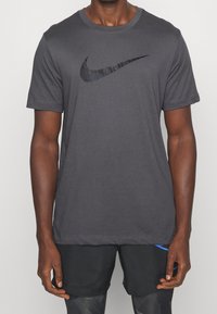 Szary T-shirt z krótkim rękawem wykonany z miękkiego materiału, z czarnym logo Nike na piersi. Posiada okrągły dekolt i standardowy krój.