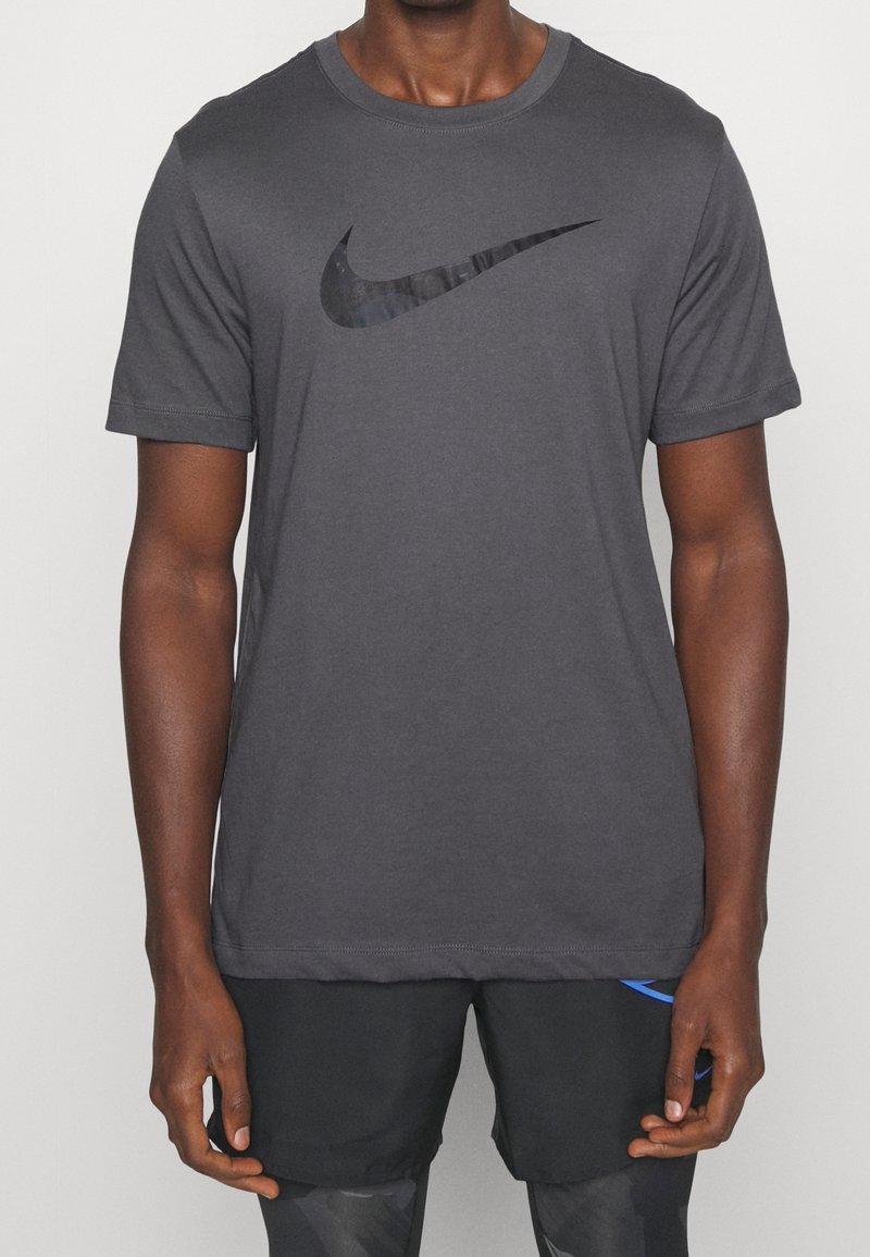 Szary T-shirt z krótkim rękawem wykonany z miękkiego materiału, z czarnym logo Nike na piersi. Posiada okrągły dekolt i standardowy krój.