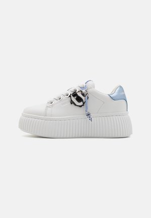 White sneaker with textured, ridged sole, featuring a blue accent at the heel and a pendant detail on the laces. Smooth leather upper.