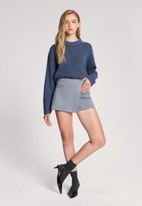 Niebieski sweter z dzianiny z prążkowanymi mankietami w połączeniu z szarym spódnicą w stylu kopertowym. Modelka nosi czarne lakierowane szpilki i ciemnoszare skarpetki. Gładkie tekstury.