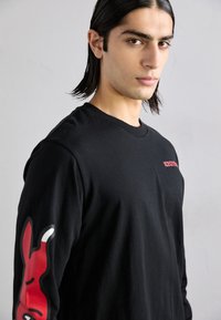 T-shirt nera a maniche lunghe con dettagli grafici rossi sulla manica sinistra e sul davanti, realizzata in cotone con una texture liscia.
