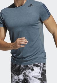 Hombre corriendo con una camiseta texturizada azul de Adidas con logo y pantalones cortos de patrón en blanco y negro, recortados en el cuello y la cintura.