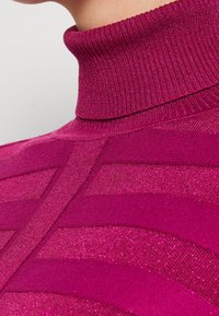 Pull en laine à col roulé de couleur magenta vif avec un motif texturé de rayures horizontales, doté d'un col côtelé et d'éléments brillants.